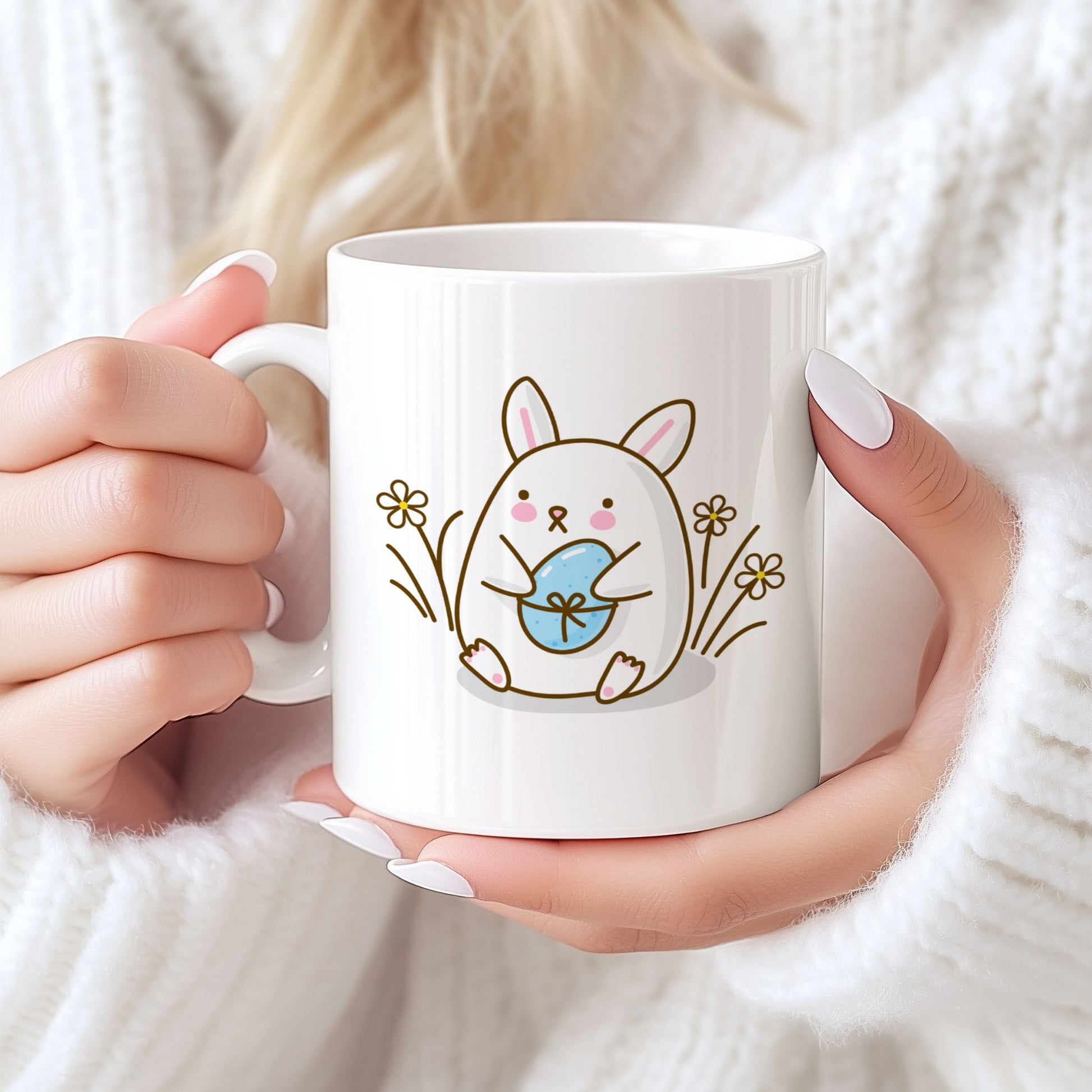 Hvitt keramikkrus med søt påskehare som holder lyseblått påskeegg og teksten God påske i blå tone på motsatt side. Person holder kruset.