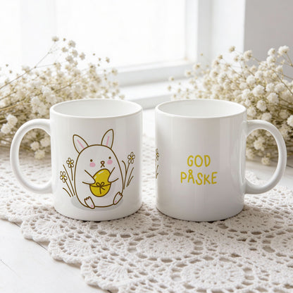 Hvitt keramikkrus med søt påskehare som holder gult påskeegg og teksten God påske på motsatt side.