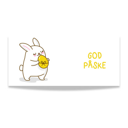 Hvitt keramikkrus med søt påskehare som holder gult påskeegg og teksten God påske i gul tone på motsatt side. Illustrasjon viser design.