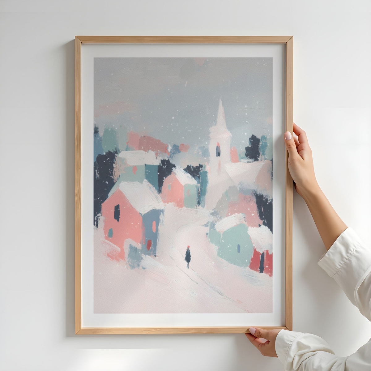 Person holder Pastel Winter Village i eikeramme med hvit kant, med snødekt landsby i rosa og blågrønne toner.