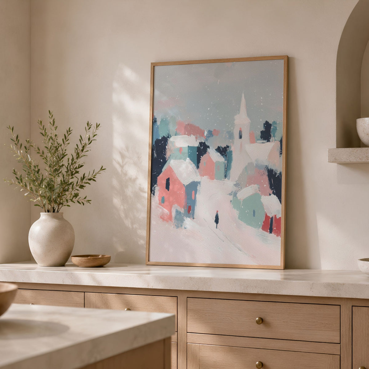 Pastel Winter Village i eikeramme plassert på lys kjøkkenbenk med keramikkvase og grønne kvister.