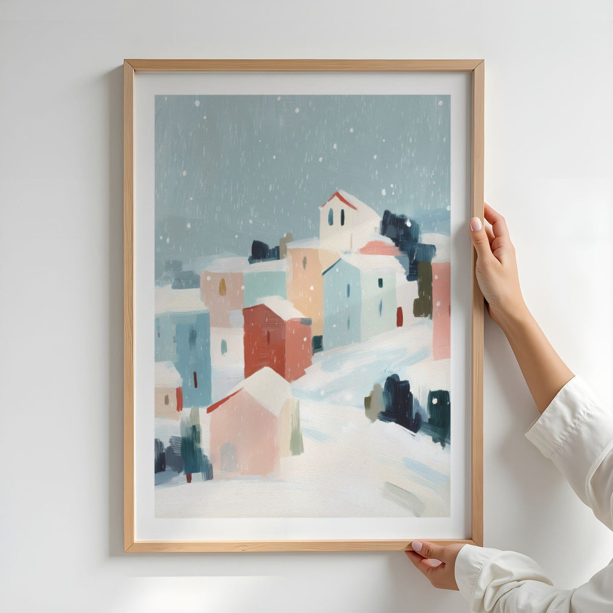 Snowfall Village vinterplakat med hvit passepartout i eikeramme, holdt opp mot lys vegg.