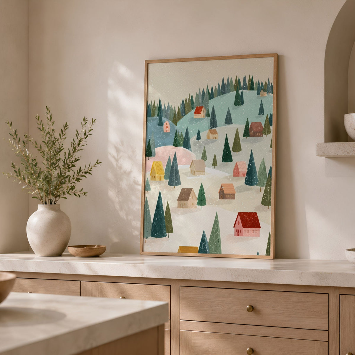 Snowy Little Village plakat i eikeramme på lys kjøkkenbenk med vase og grønne grener