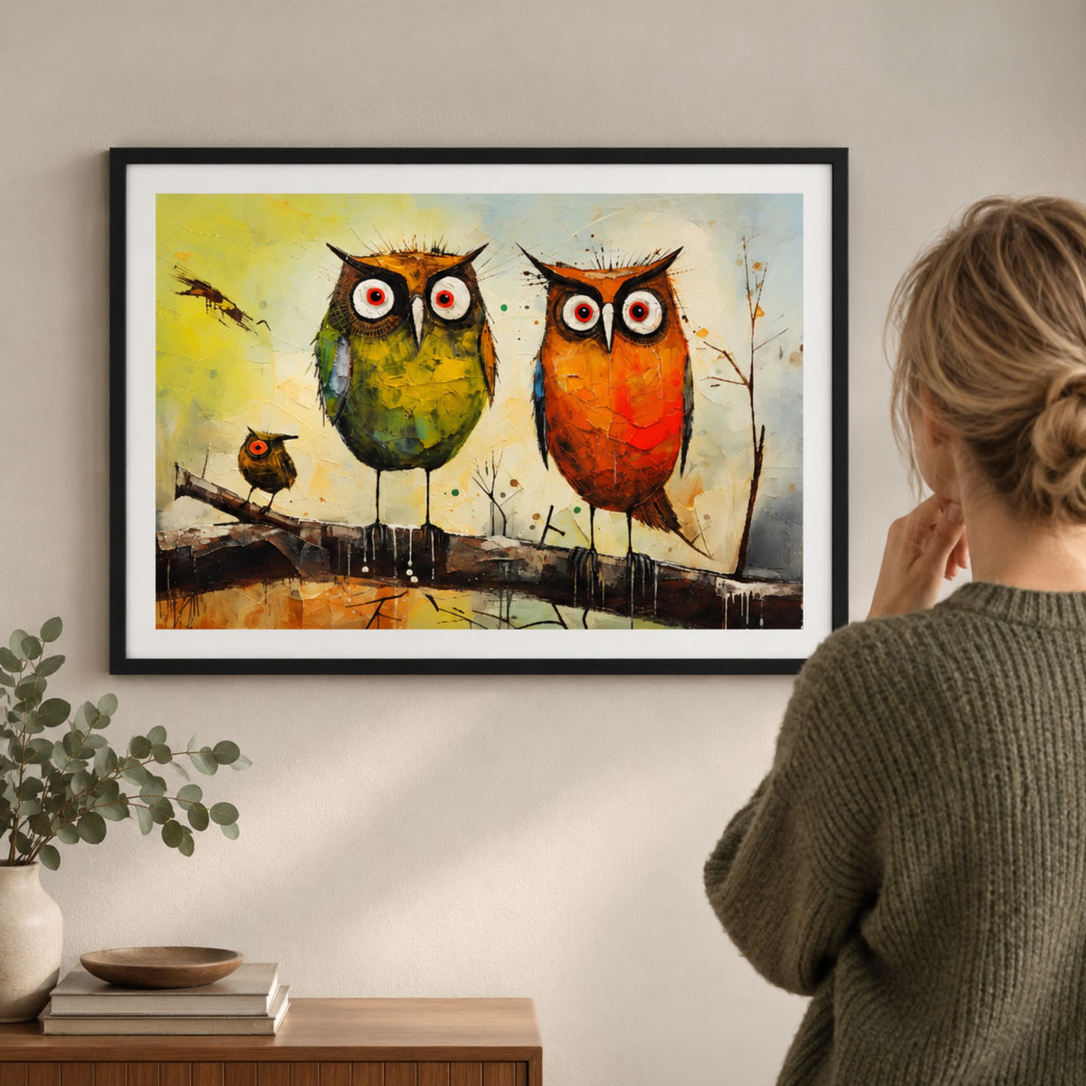 Kvinne betrakter fargerik kunstplakat med to store ugler og en liten ugle i sort ramme