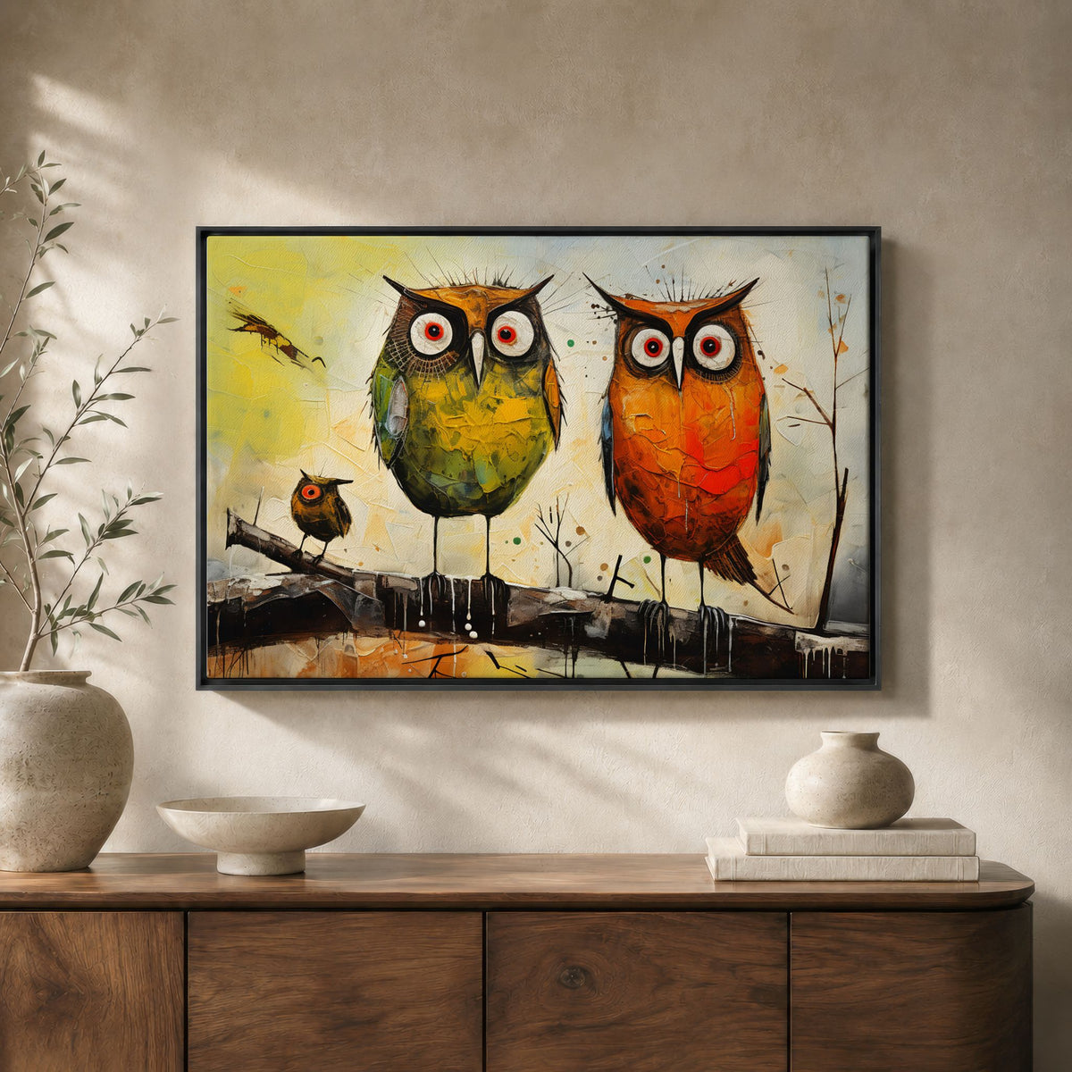 Kunstplakat med to store ugler og en liten ugle uten hvit kant i sort ramme over skjenk i tre