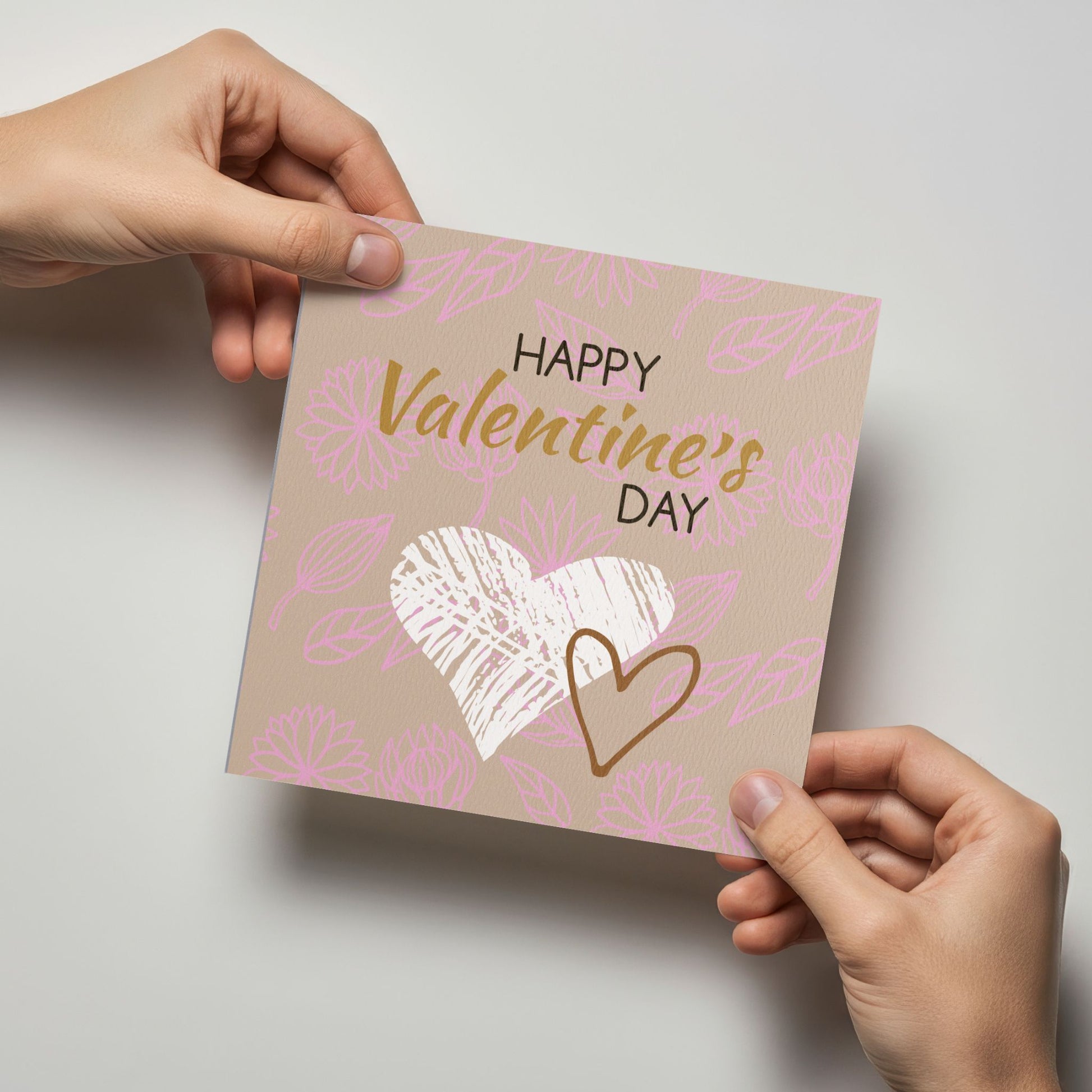 Valentineskort med teksten Happy Valentine’s Day, håndtegnede hjerter og floralt mønster i beige og rosa toner. Kortet blir holdt av en person.