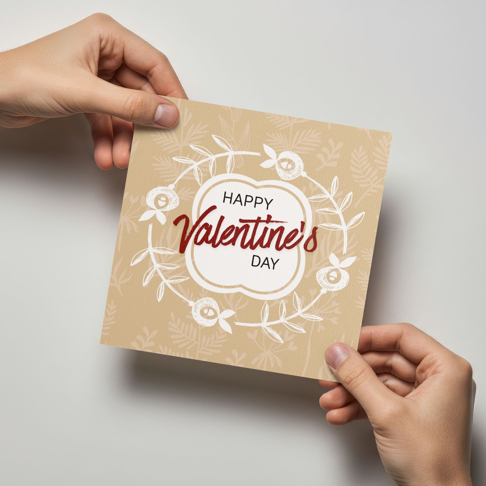 Valentineskort med teksten Happy Valentine’s Day, dekorativ blomsterkrans og botaniske detaljer i varme beige toner. Kortet blir holdt av en person.