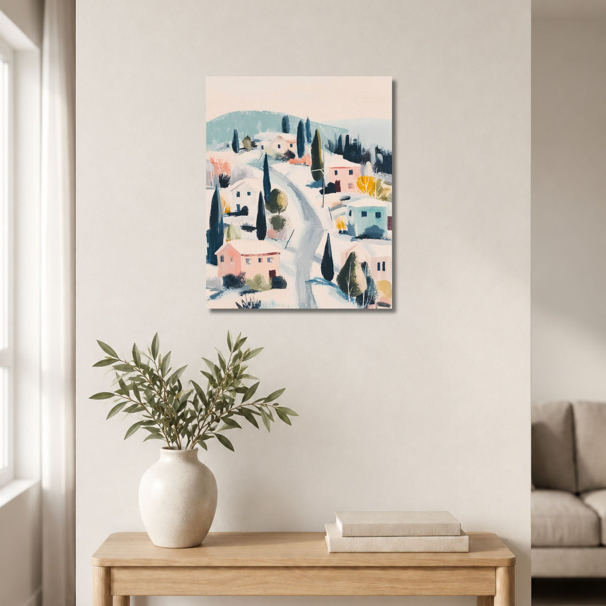 Vertikalt lerretsbilde med malerisk vinterlandsby over lyst trebord med keramikkvase og bøker.