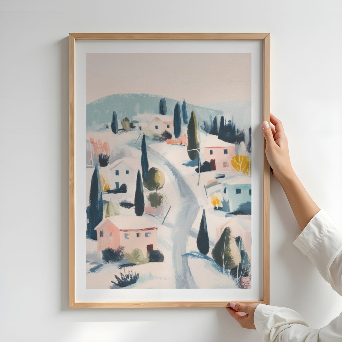 Winter Village vinterplakat med hvit passepartout i eikeramme, holdt opp mot lys vegg.