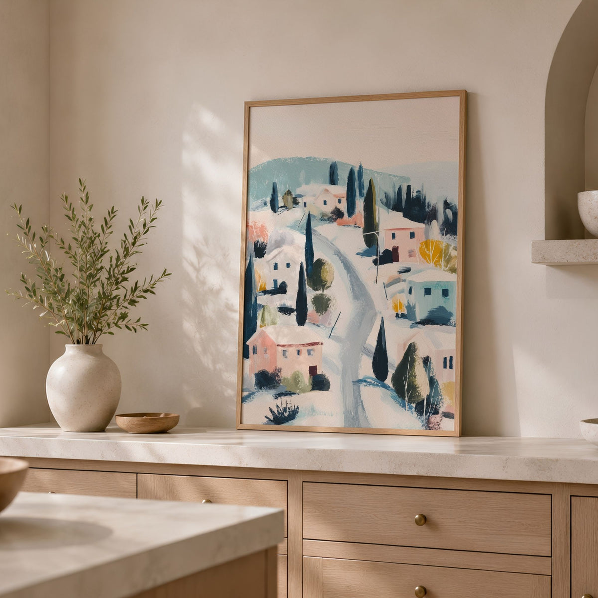 Winter Village plakat i eikeramme plassert på lys kjøkkenbenk med grønne grener i vase.