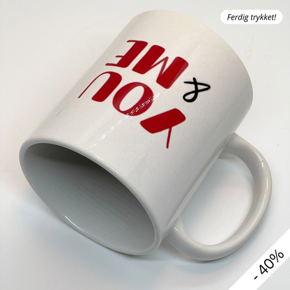Krus i keramikk med teksten "YOU & ME" og en dristig typografi med et rødt fingeravtrykk-hjerte.